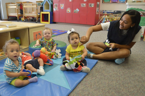 A teacher and three babies play on the floor