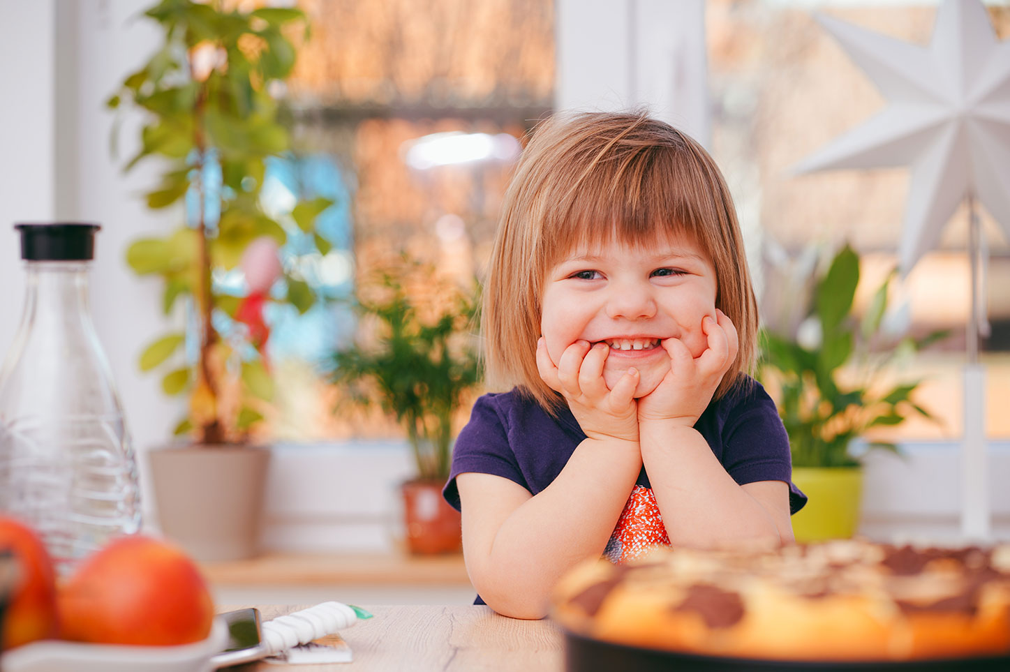 smiling toddler in kitchen with blurred pizza